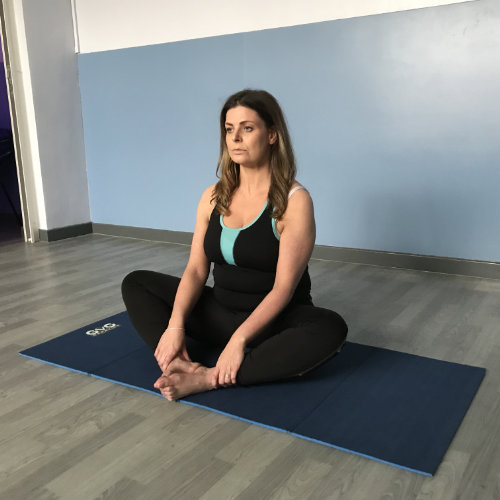 A pregnant person with long hair in a sitting yoga pose